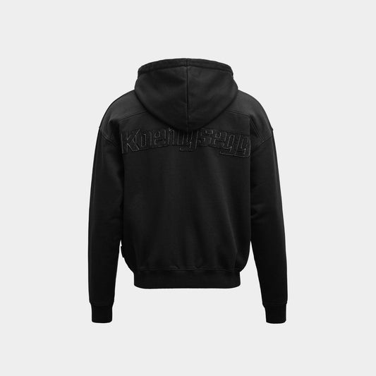 A black zipped hoodie shown from the back, featuring a tonal black embroidered 'Koenigsegg' logo across the upper back, set against a plain light gray background.