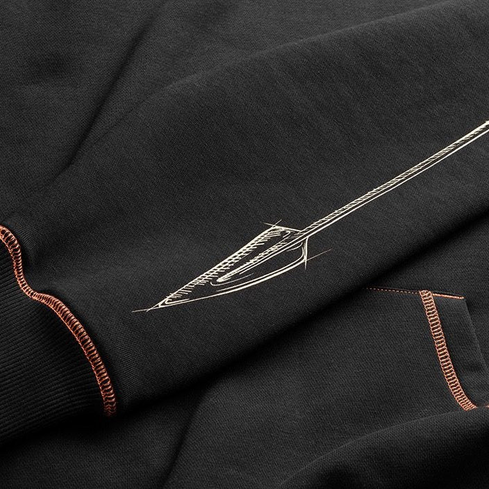 Close-up of a black hoodie featuring a detailed white spear graphic on the sleeve, accented by orange contrast stitching on the ribbed cuffs and pocket.