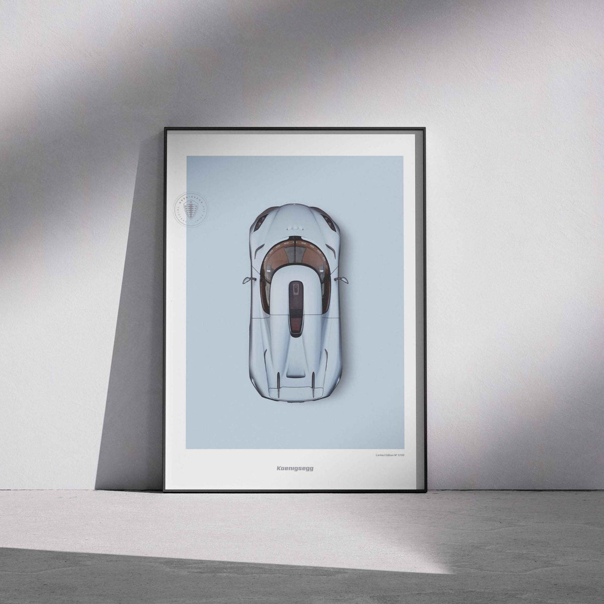 A framed art print featuring a top-down illustration of a blue Regera on a light blue background, leaning against a gray wall on a concrete floor with dramatic shadows.