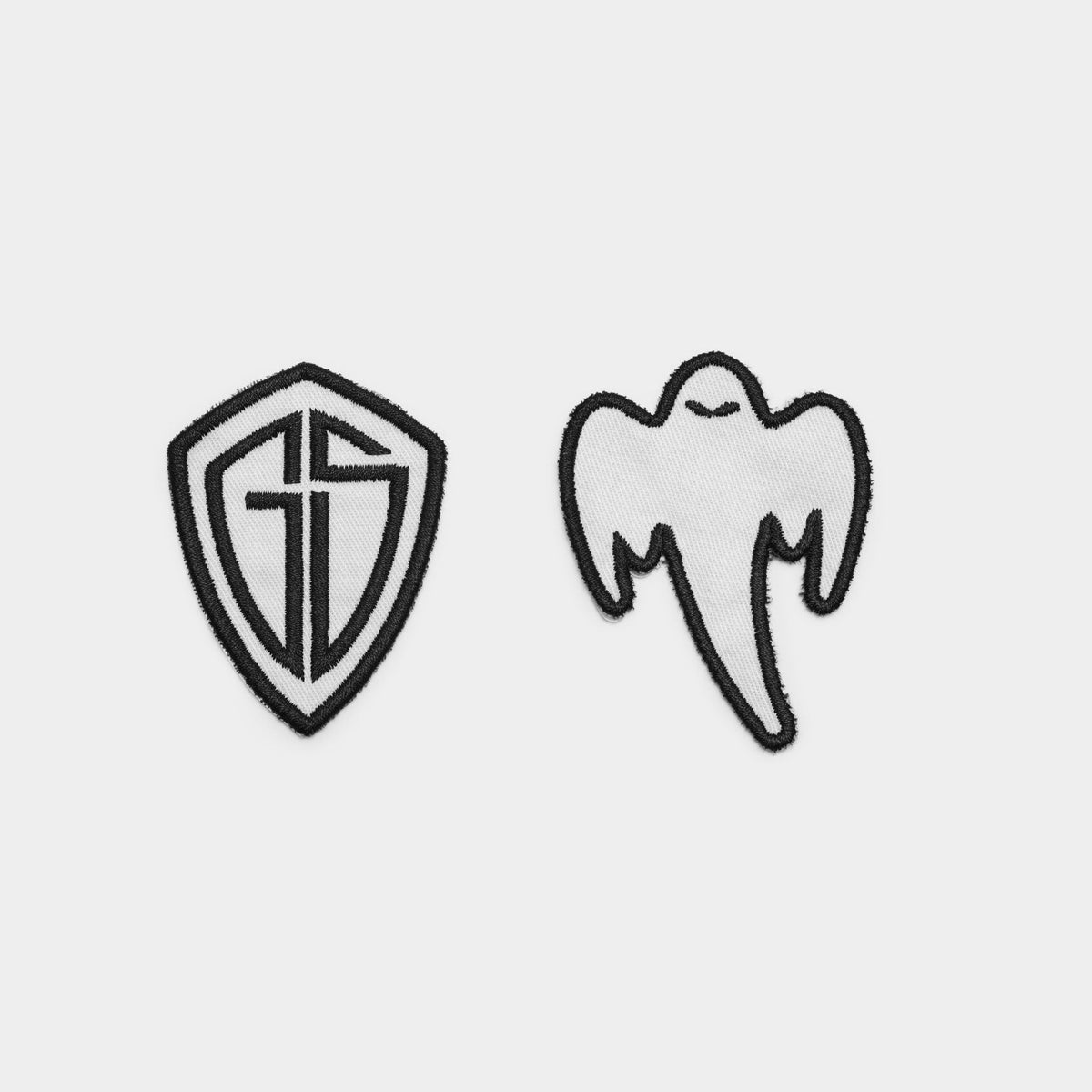 Two small embroidered patches on a light gray background: a shield patch  and a ghost patch with wings and a long tail, both outlined in black.