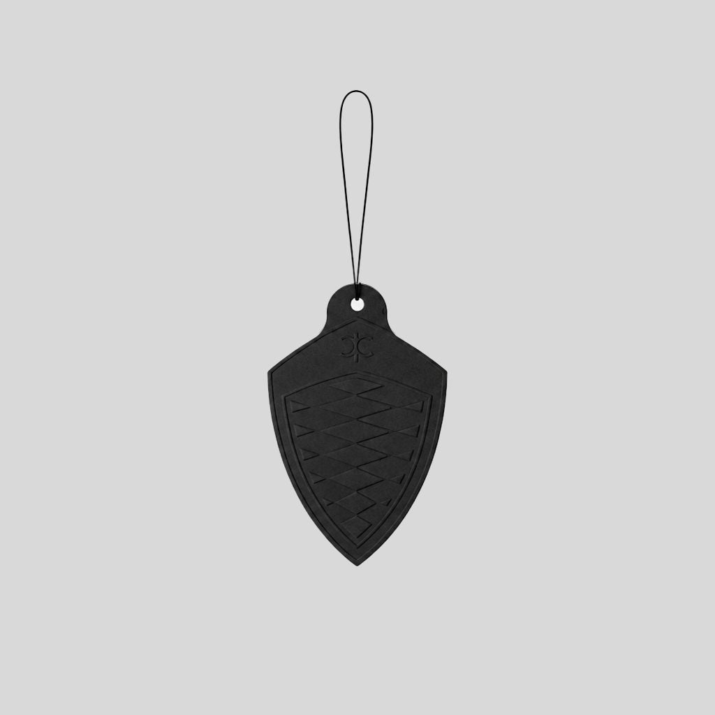 A black shield-shaped car air freshener tag with a hanging loop, shown against a solid light gray background.