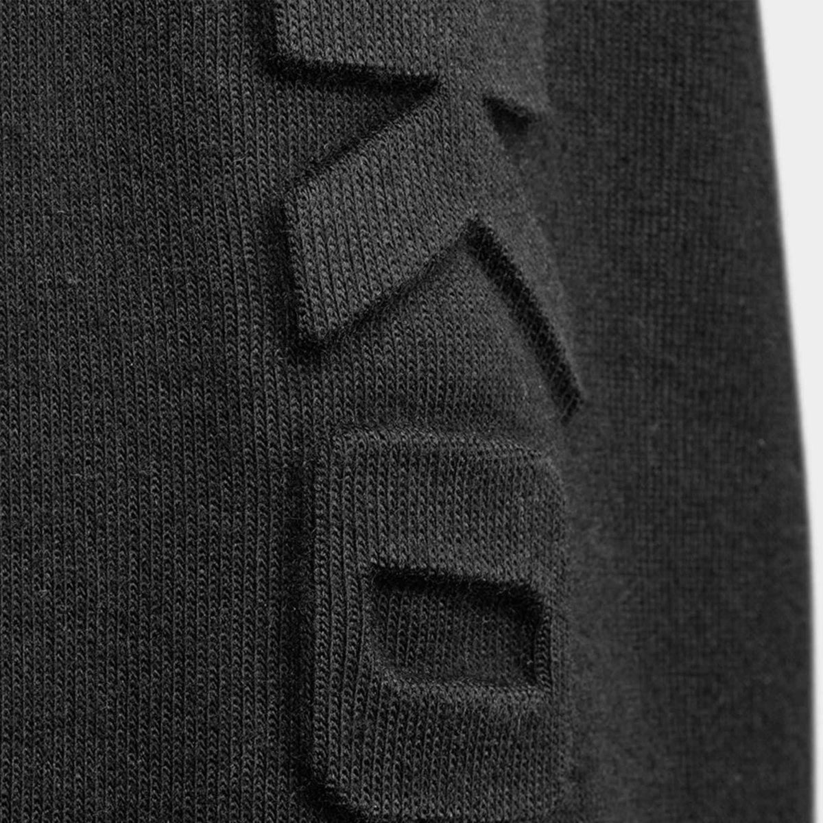 Close-up of a black ribbed knit garment featuring a large, tonal geometric logo patch on the front.