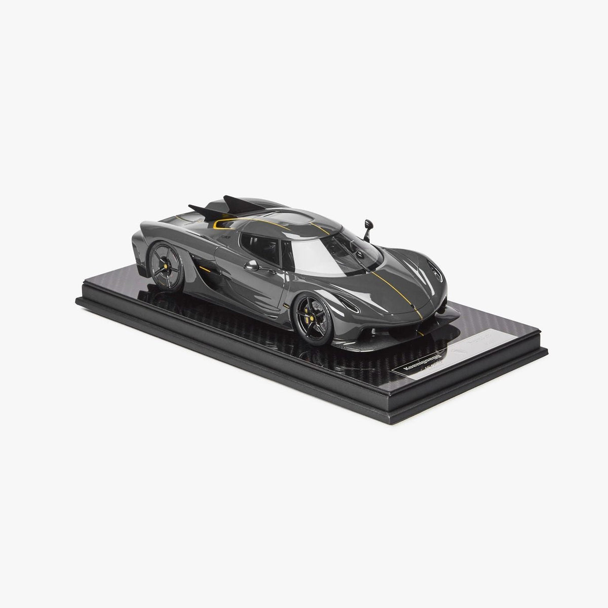 A scale model of a dark gray and black Jesko Absolut with yellow accents, displayed on a black base against a clean white background.