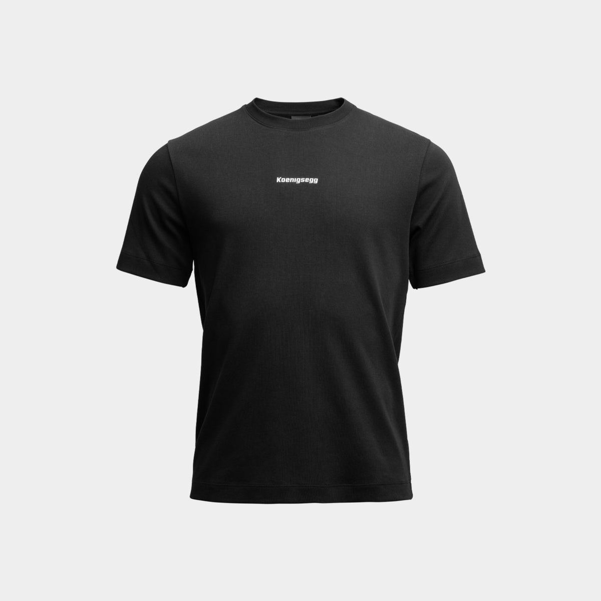 A black short-sleeve crewneck t-shirt with a small white 'Koenigsegg' logo printed on the chest, displayed against a light gray background.