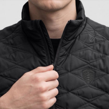 Close-up of a person wearing a black diamond-quilted Koenigsegg zip-up jacket, pulling the zipper with one hand. A small shield logo is visible on the left chest.