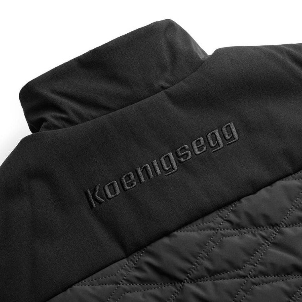 Close-up of a black Koenigsegg jacket showing the brand name embroidered on the shoulder and a quilted texture below.
