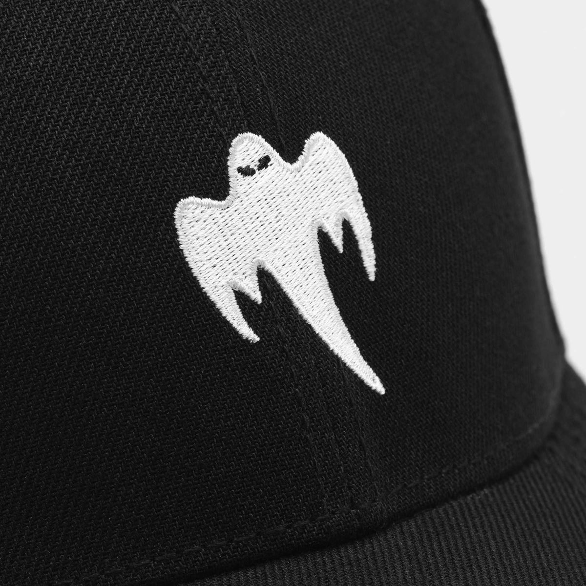 Close-up of a black baseball cap featuring a white embroidered ghost logo on the front panel.