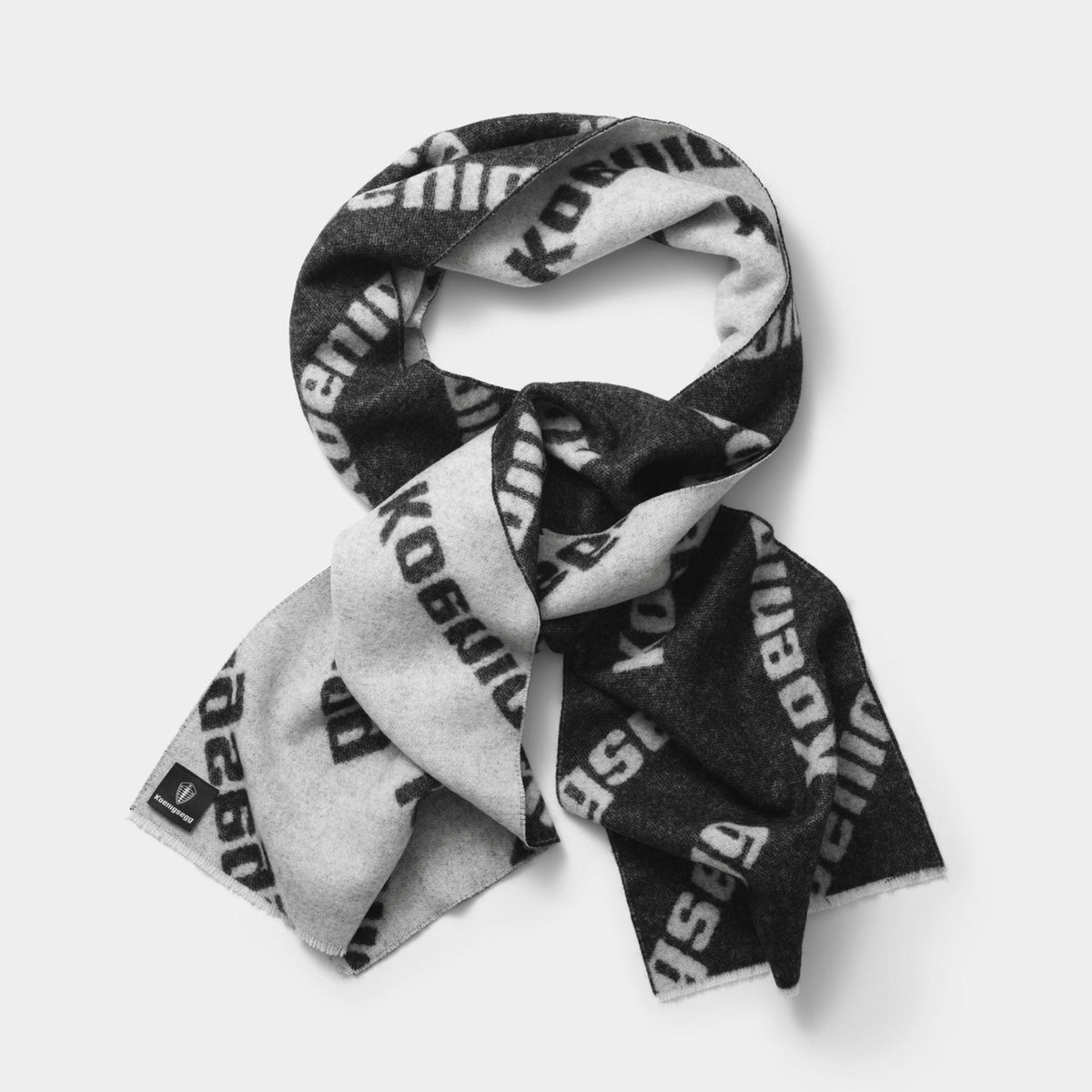 A black and light gray scarf with a repeating 'Koenigsegg' text pattern, styled in a loose loop on a light gray background.