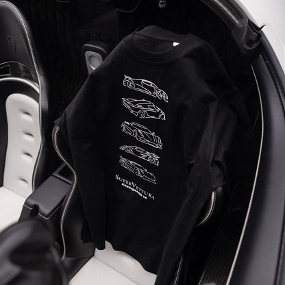 A black crewneck sweatshirt featuring white line-art illustrations of sports cars and the text 'SUPERVETTURA' printed on the back, draped over the seat of a Koenigsegg car interior.