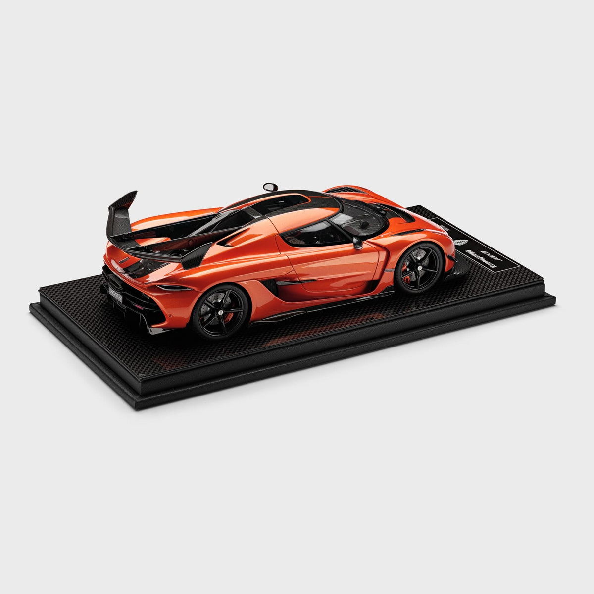A metallic orange and black scale model of a Koenigsegg Jesko Attack on a black display base, photographed against a solid light gray background.