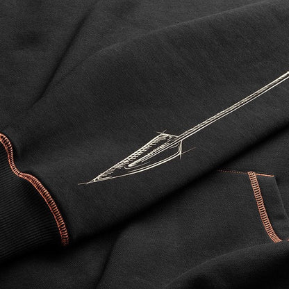 Close-up of a black hoodie featuring a detailed white spear graphic on the sleeve, accented by orange contrast stitching on the ribbed cuffs and pocket.