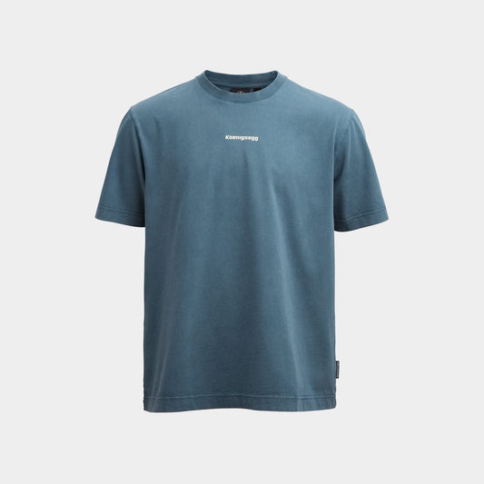 A slate blue short-sleeve crewneck t-shirt with a small white 'Koenigsegg' logo printed on the center chest, displayed against a light gray background.
